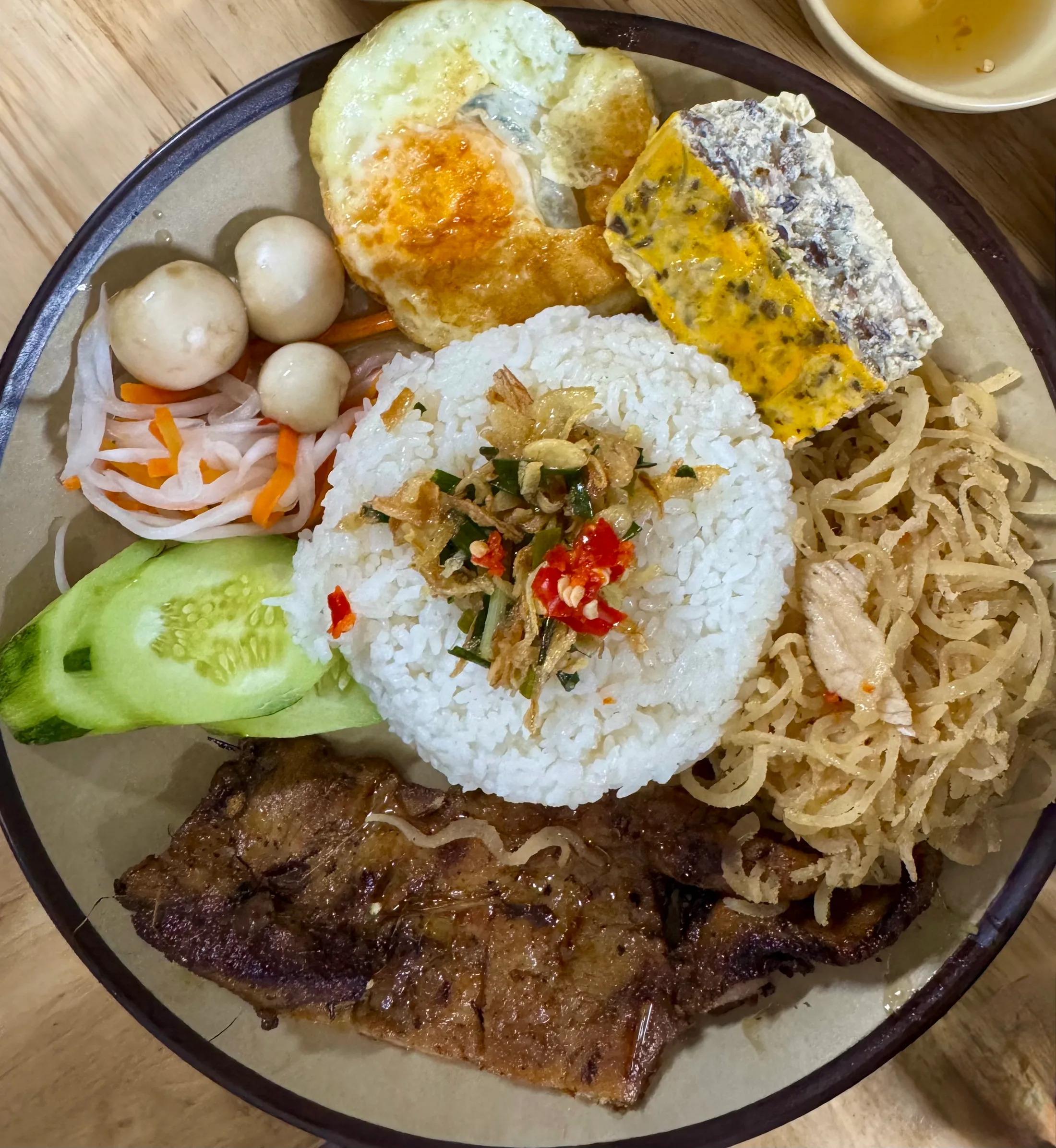 A plate of cơm tấm — broken rice with grilled pork, a fried egg and pickled vegetables
