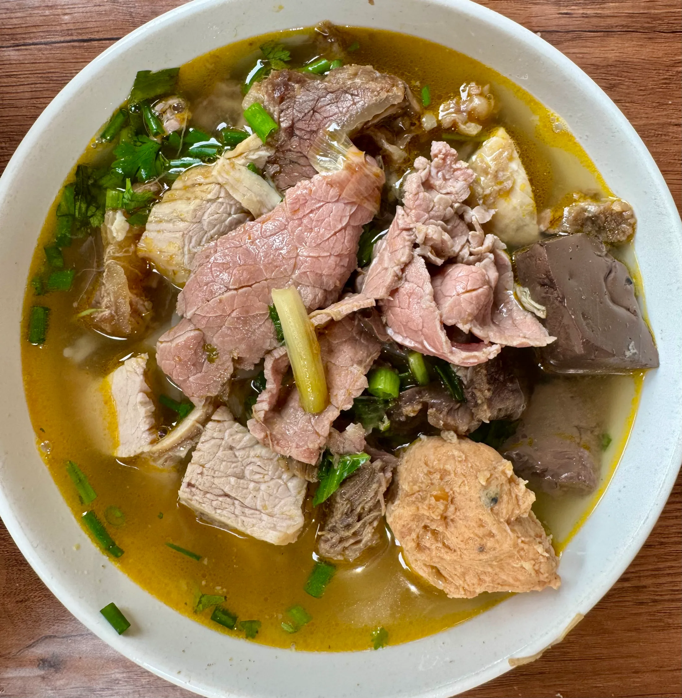A bowl of bún bò Huế, sliced beef and herbs in a golden broth