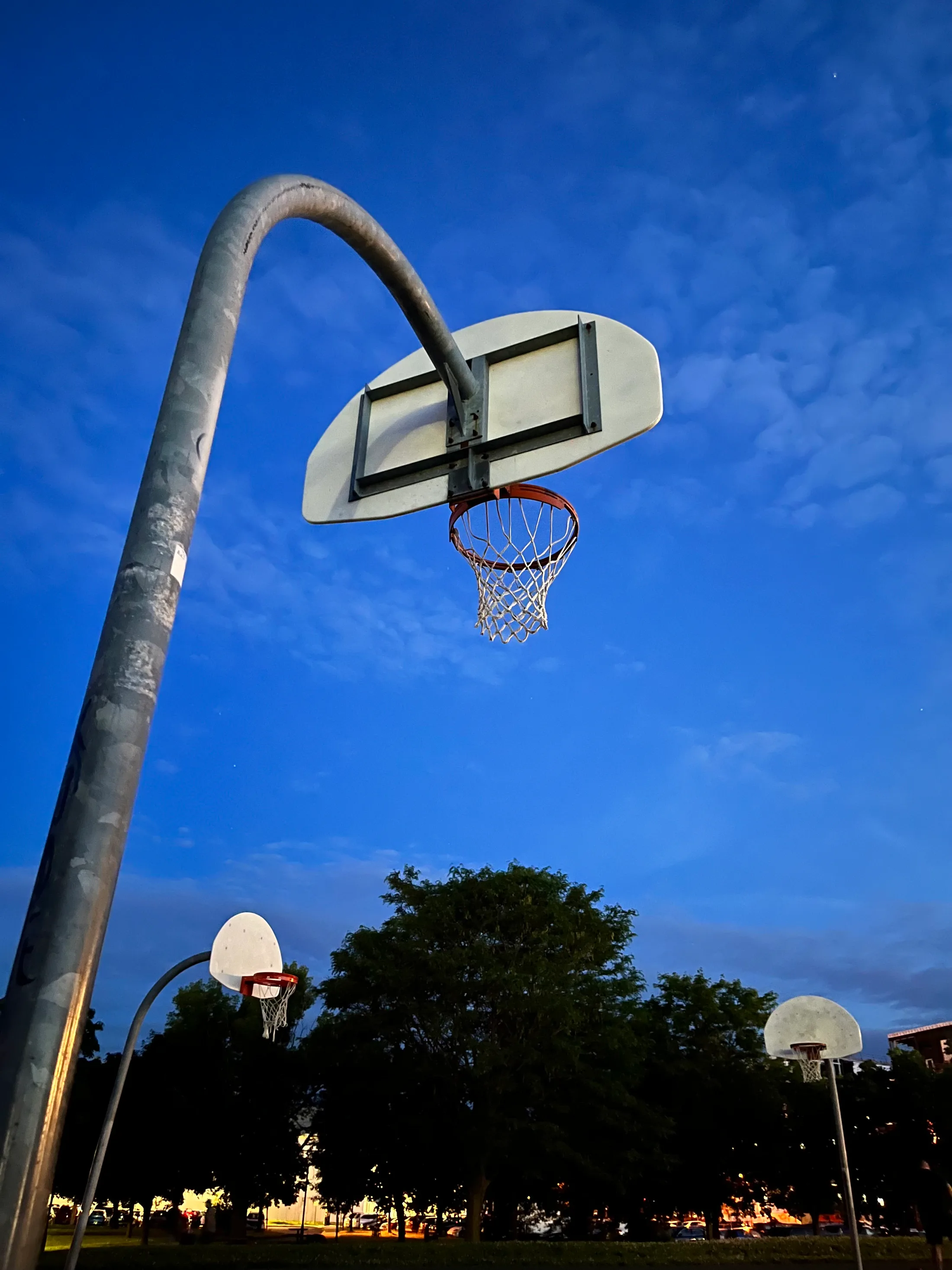 A basketball hoop shot from below against a deep blue evening sky