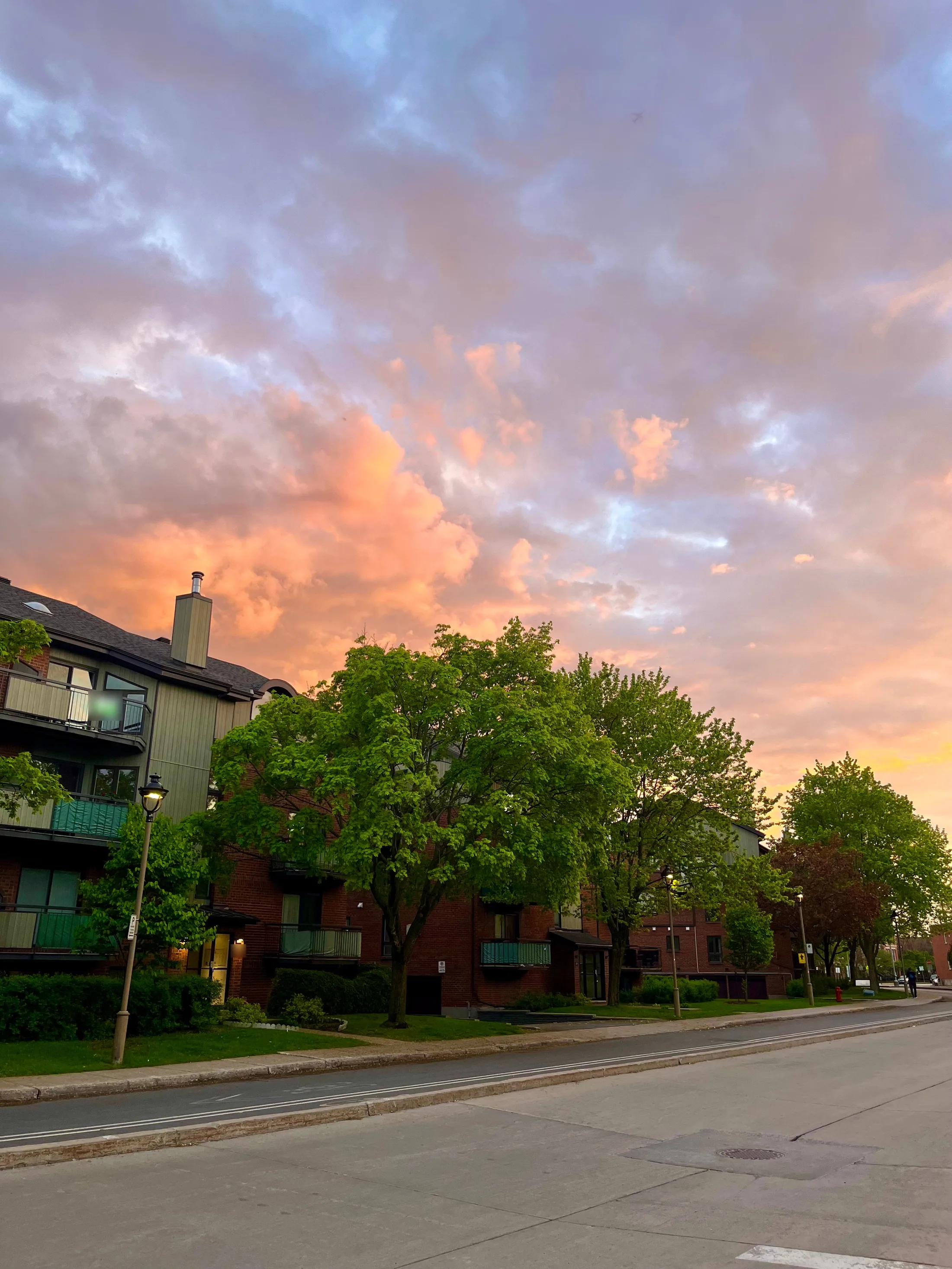 Pink and grey clouds at sunset over a brick apartment block and its balconies on a quiet Montréal street