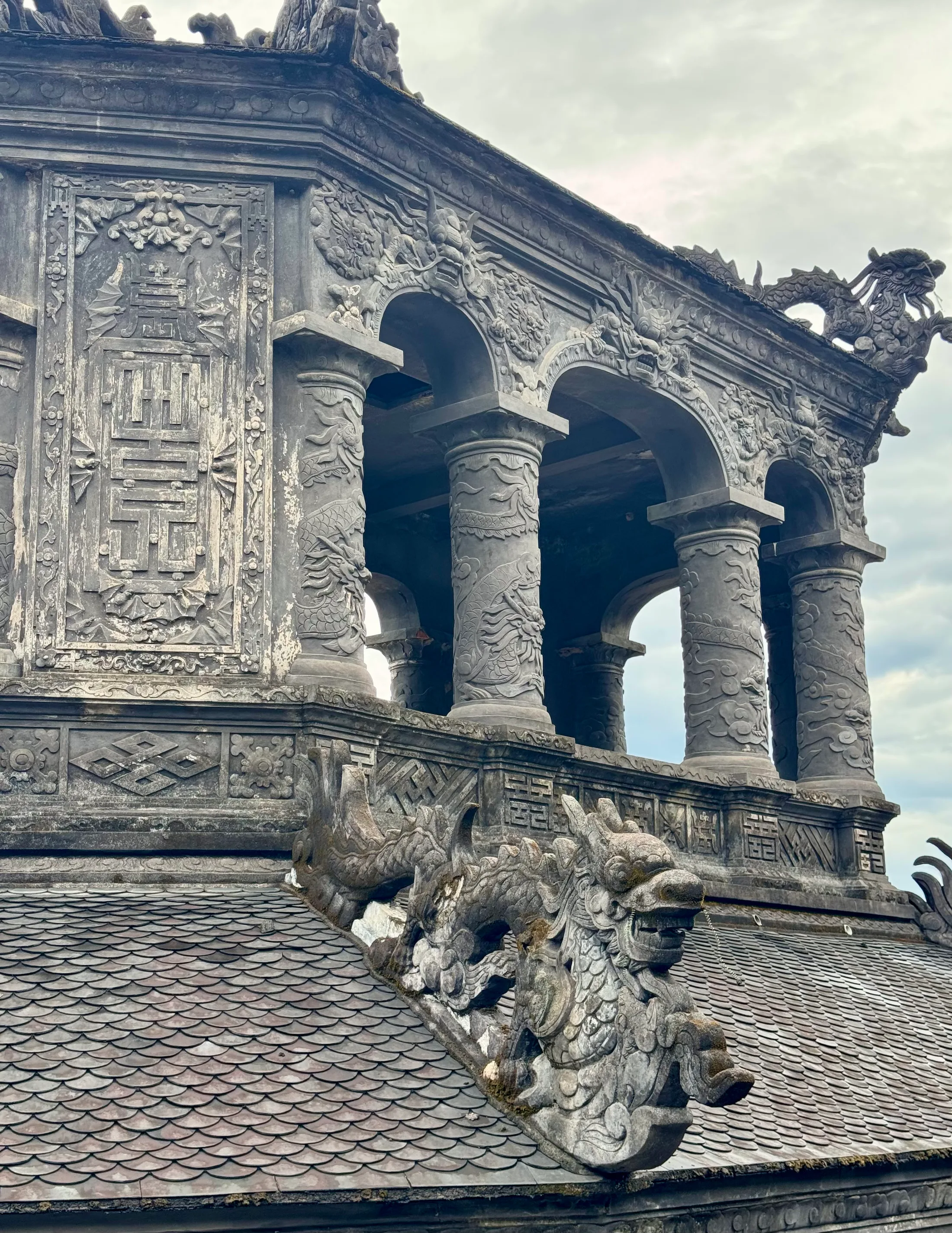 A carved dragon on the tiled roofline of a royal tomb in Huế, stone weathered grey