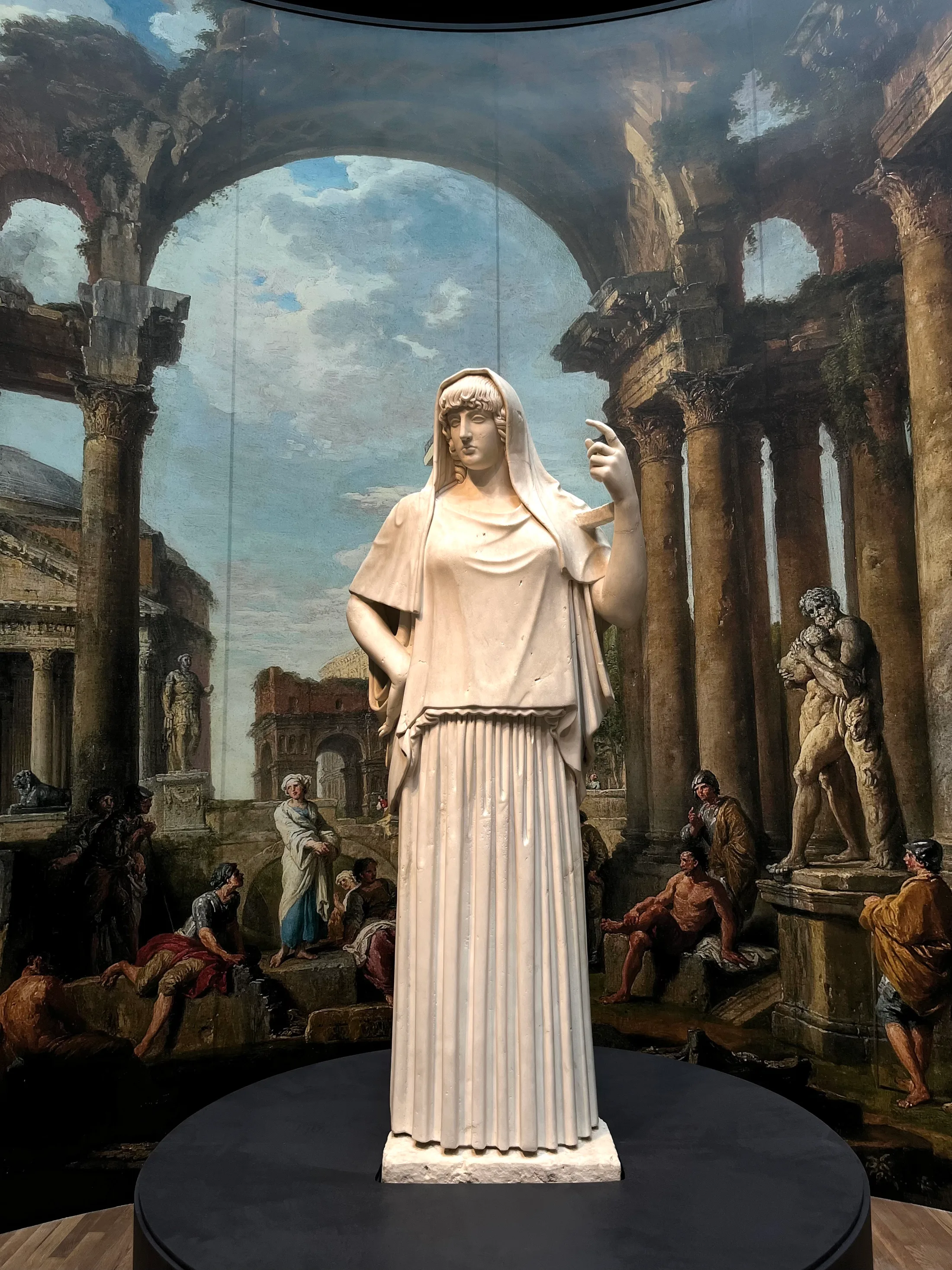A marble statue of a veiled woman standing before a painted backdrop of Roman ruins and figures